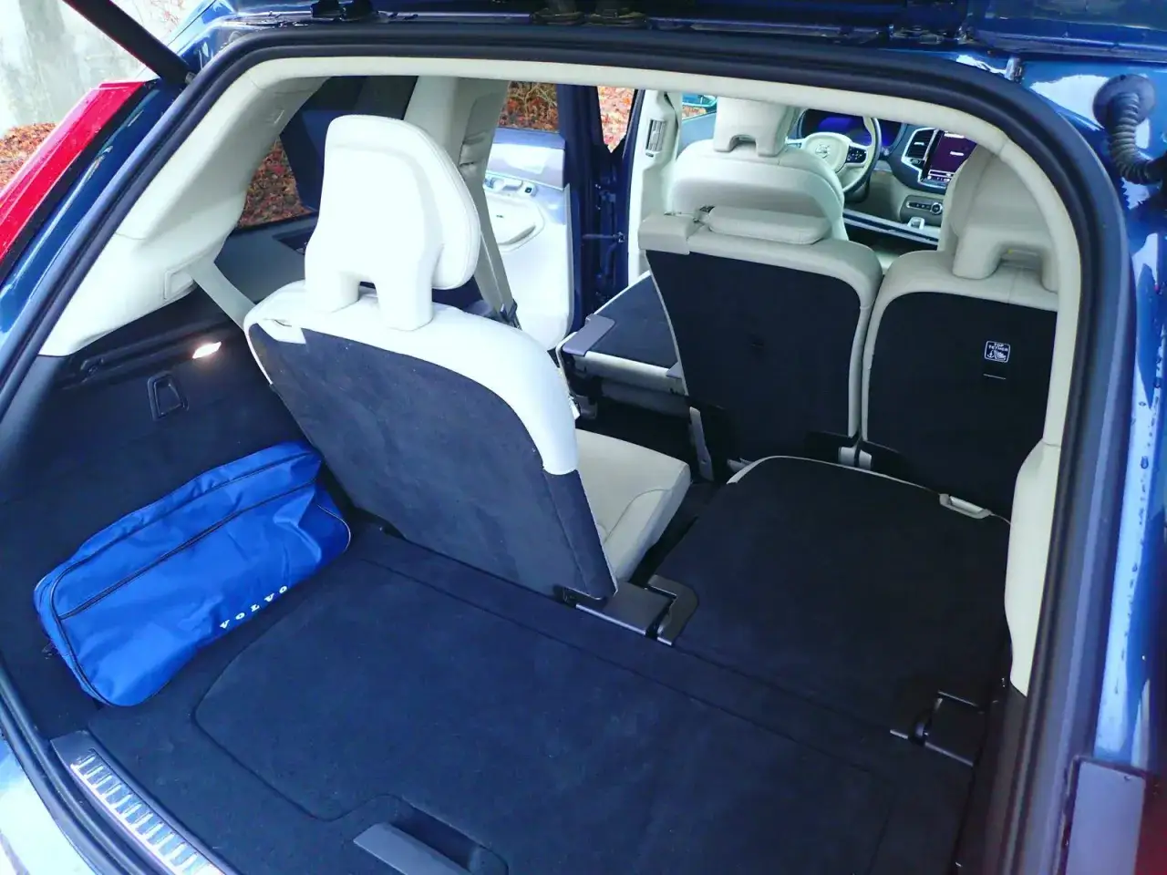 Wnętrze Volvo XC90 z rozłożonymi siedzeniami i niebieską torbą z logo Volvo.