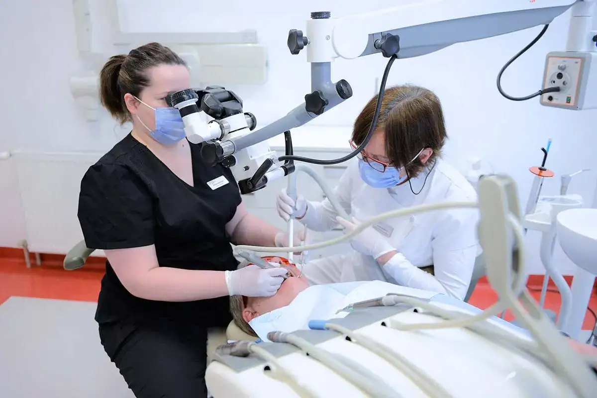 Dwie dentystki wykonują leczenie kanałowe pod mikroskopem. Poznaj leczenie kanałowe cena i dowiedz się, jak dbać o zdrowie zębów.