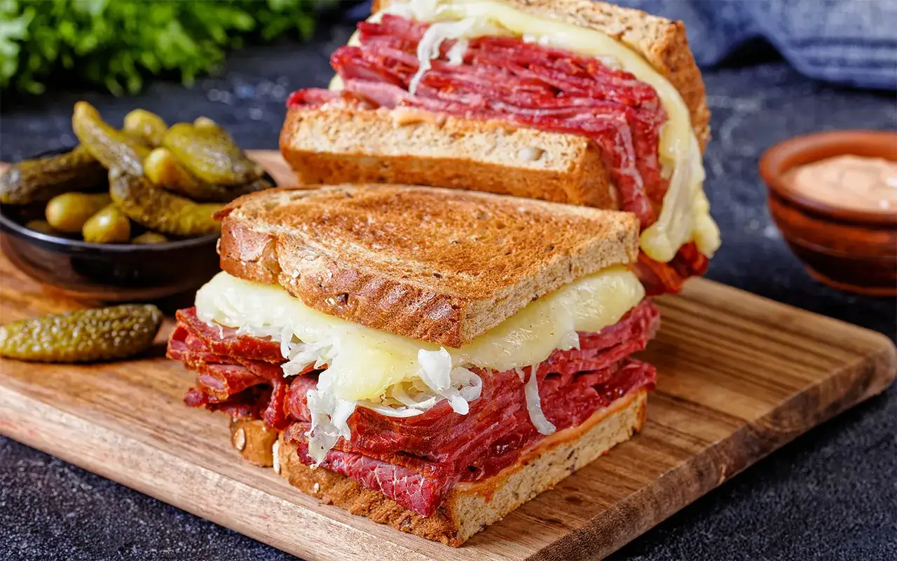 Två saftiga reuben sandwiches med ost som smälter, serverade med saltgurka och en dippsås.