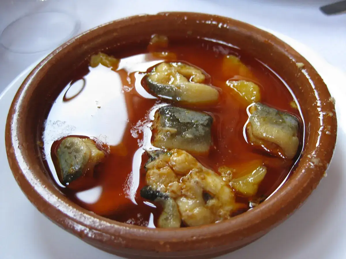 Un cuenco de barro con trozos de anguila en una salsa rojiza. Un plato tradicional de all i pebre, listo para ser disfrutado.