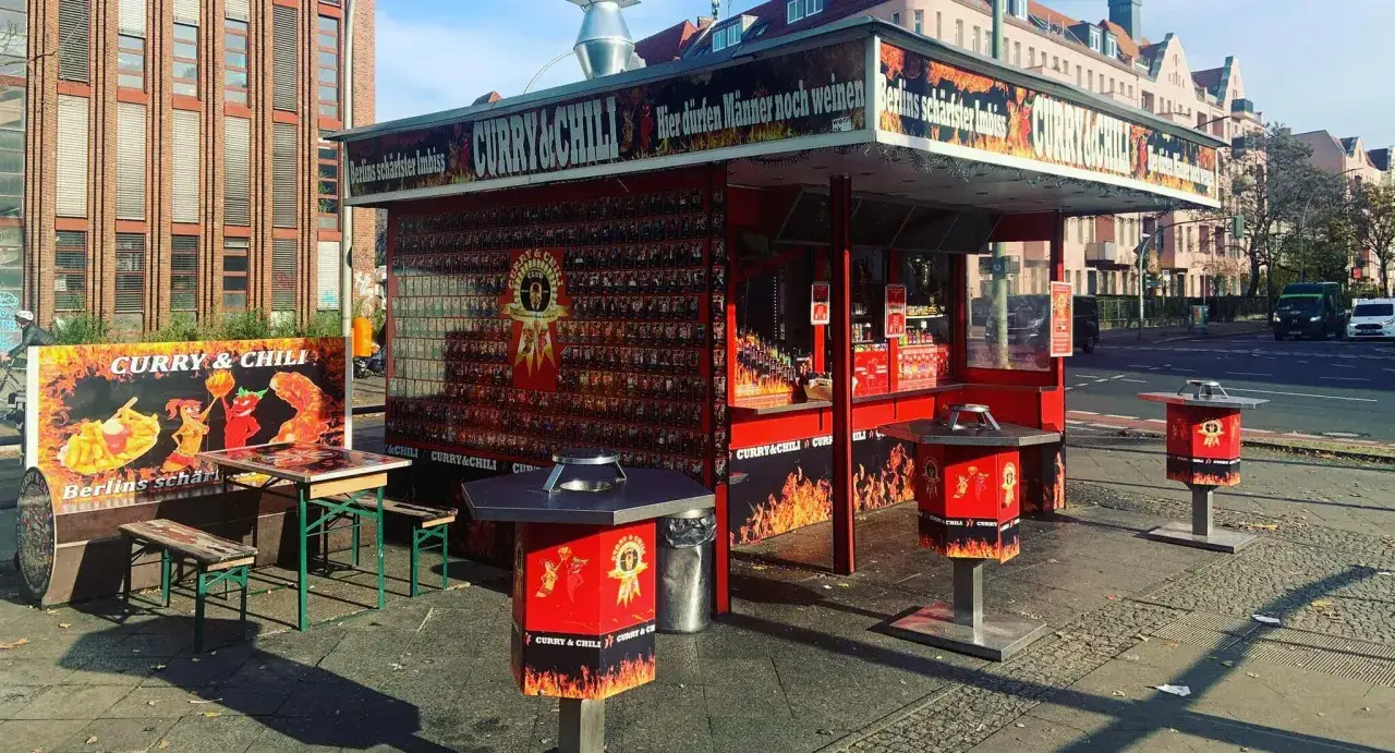 Berliner Imbiss mit Currywurst und Chili. Die Fassade ist mit Bildern und dem Slogan 