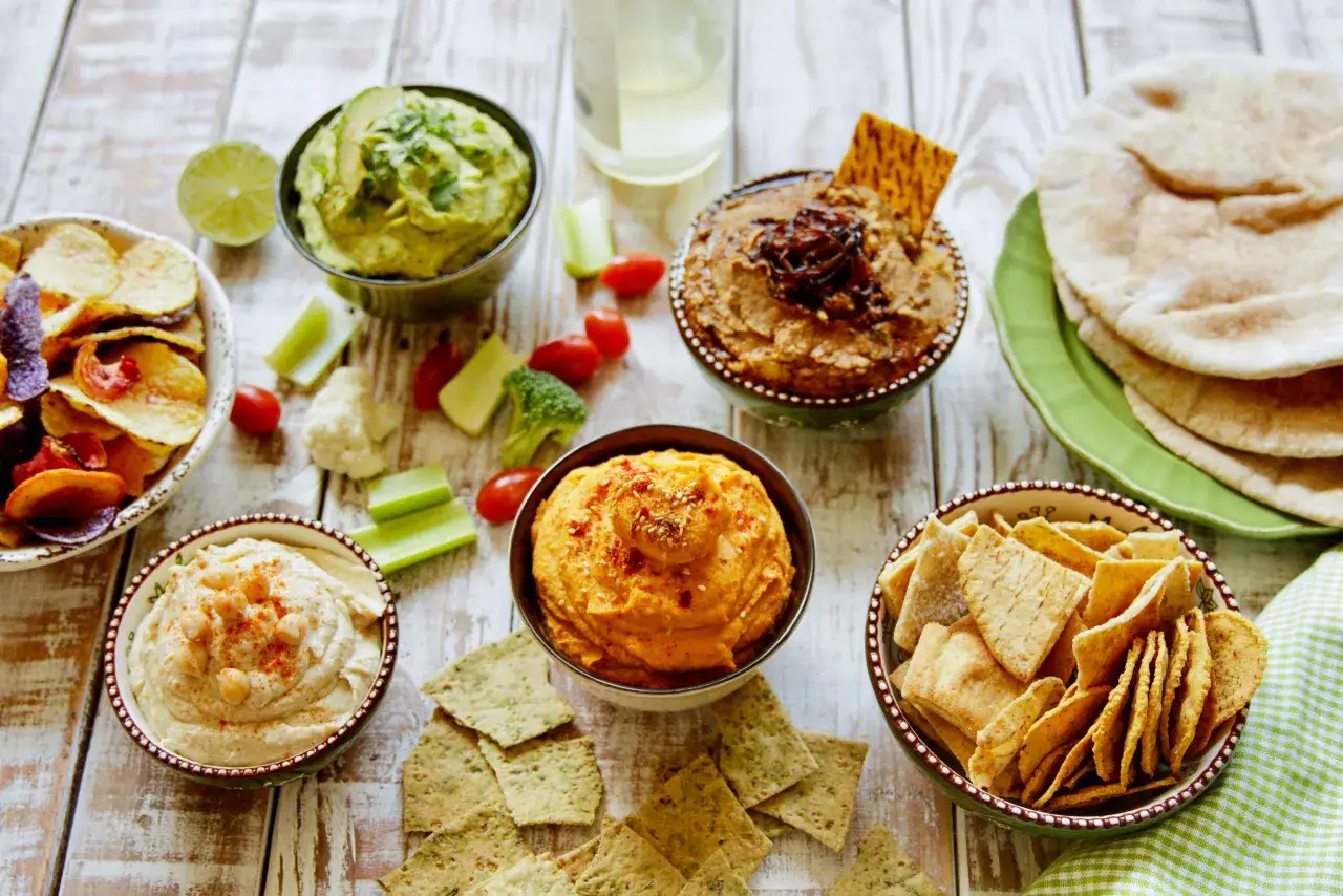 Variedad de hummus y acompañamientos, perfectos para tus recetas de hummus. Incluye chips, pan de pita y vegetales frescos.