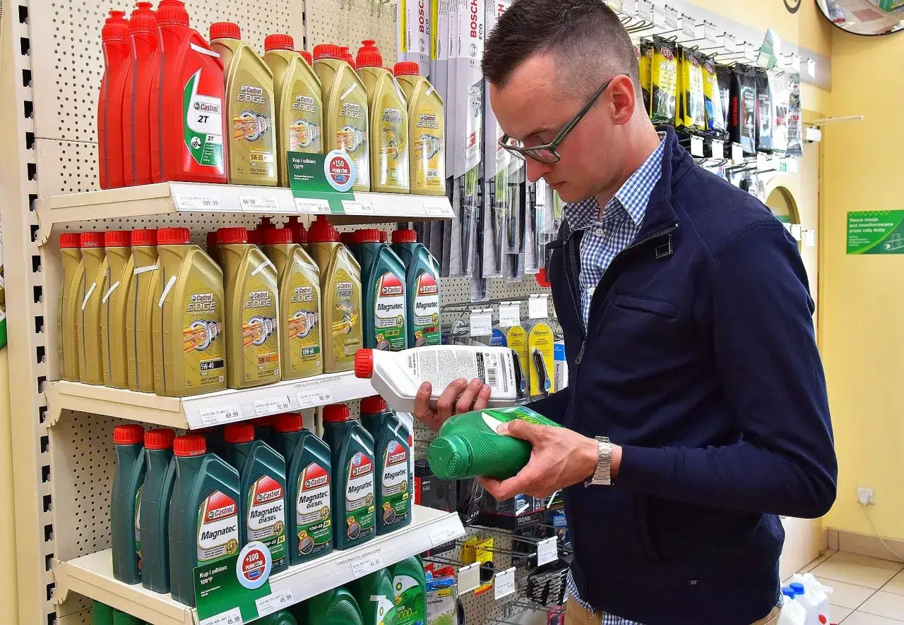 Mężczyzna w sklepie motoryzacyjnym zastanawia się, czy można mieszać oleje silnikowe, porównując różne produkty Castrol.