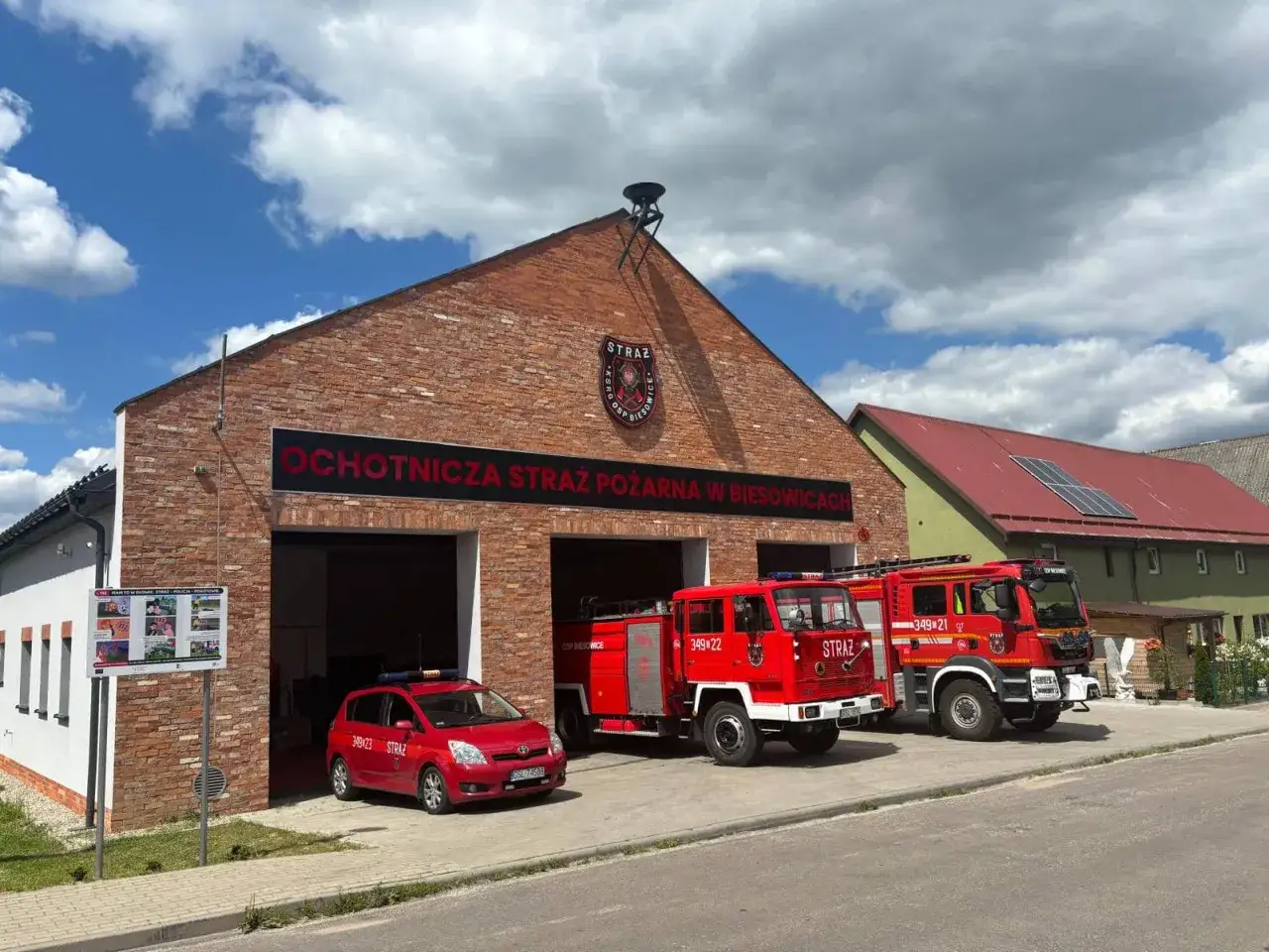 Strażak OSP w Biesowicach gotowy do akcji. Przed remizą stoją trzy wozy strażackie i czerwony samoch&oacute;d.