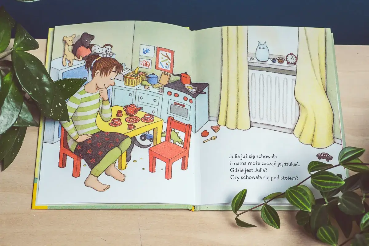 Ilustracja z książki dla 5 latki: dziewczynka bawi się w chowanego w kuchni. Mama szuka Julii.