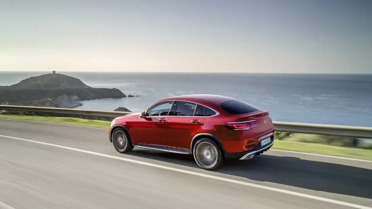 Czerwony Mercedes GLC Coupe sunie po nadmorskiej drodze. Jego dynamiczne linie podkreślają sportowy charakter, a kompaktowe mercedes glc wymiary sprawiają, że jest idealny do miejskiej dżungli i wakacyjnych podróży.
