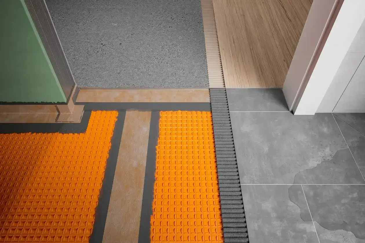 Detailansicht einer Abdichtung auf alten Fliesen mit orangefarbener Noppenbahn und angrenzendem Holzboden sowie grauen Fliesen.