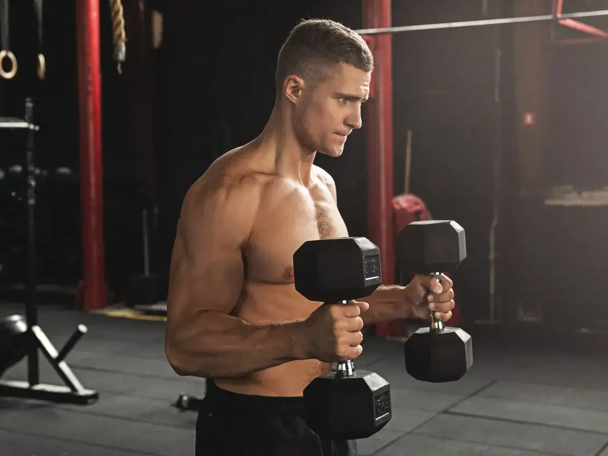 Mann trainiert Bizeps mit Hanteln im Fitnessstudio. Fokus auf Muskelaufbau und Kraftsteigerung.