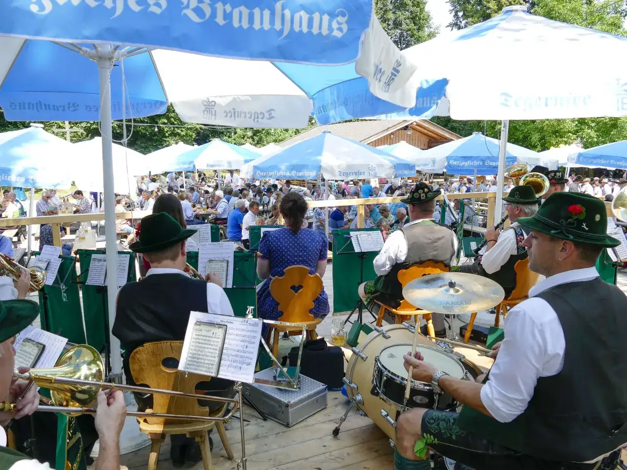 Blaskapelle spielt auf einem Waldfest in Bayern unter blau-wei&szlig;en Schirmen. G&auml;ste genie&szlig;en die Musik und das bayerische Ambiente.