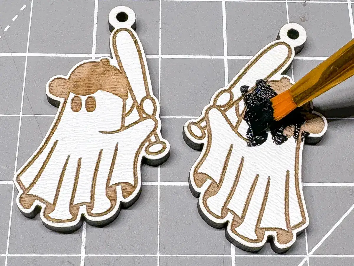 A paintbrush applies black paint to a laser-engraved ghost holding a baseball bat, demonstrating how to color laser engraving.