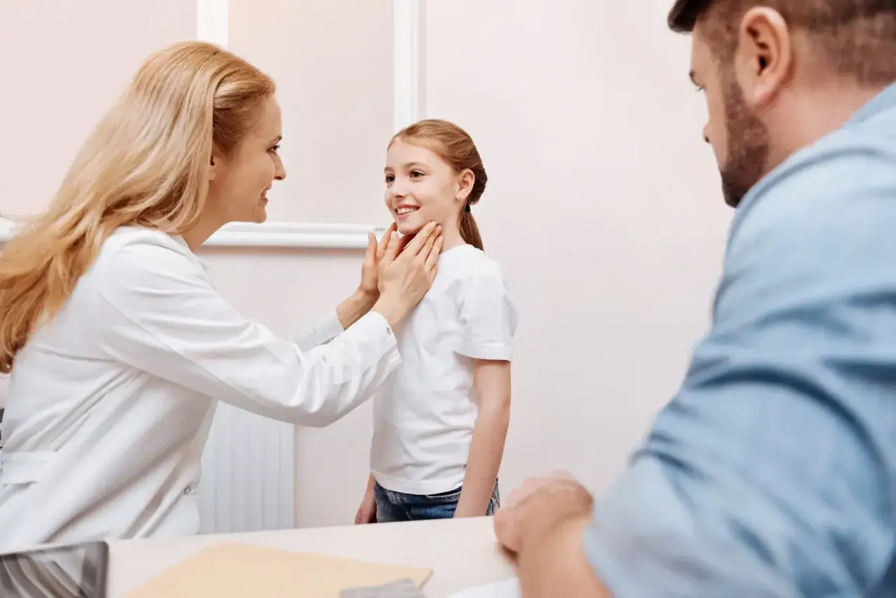 Lekarka bada szyję dziewczynki, wyjaśniając rodzicom, czym są badania immunologiczne.