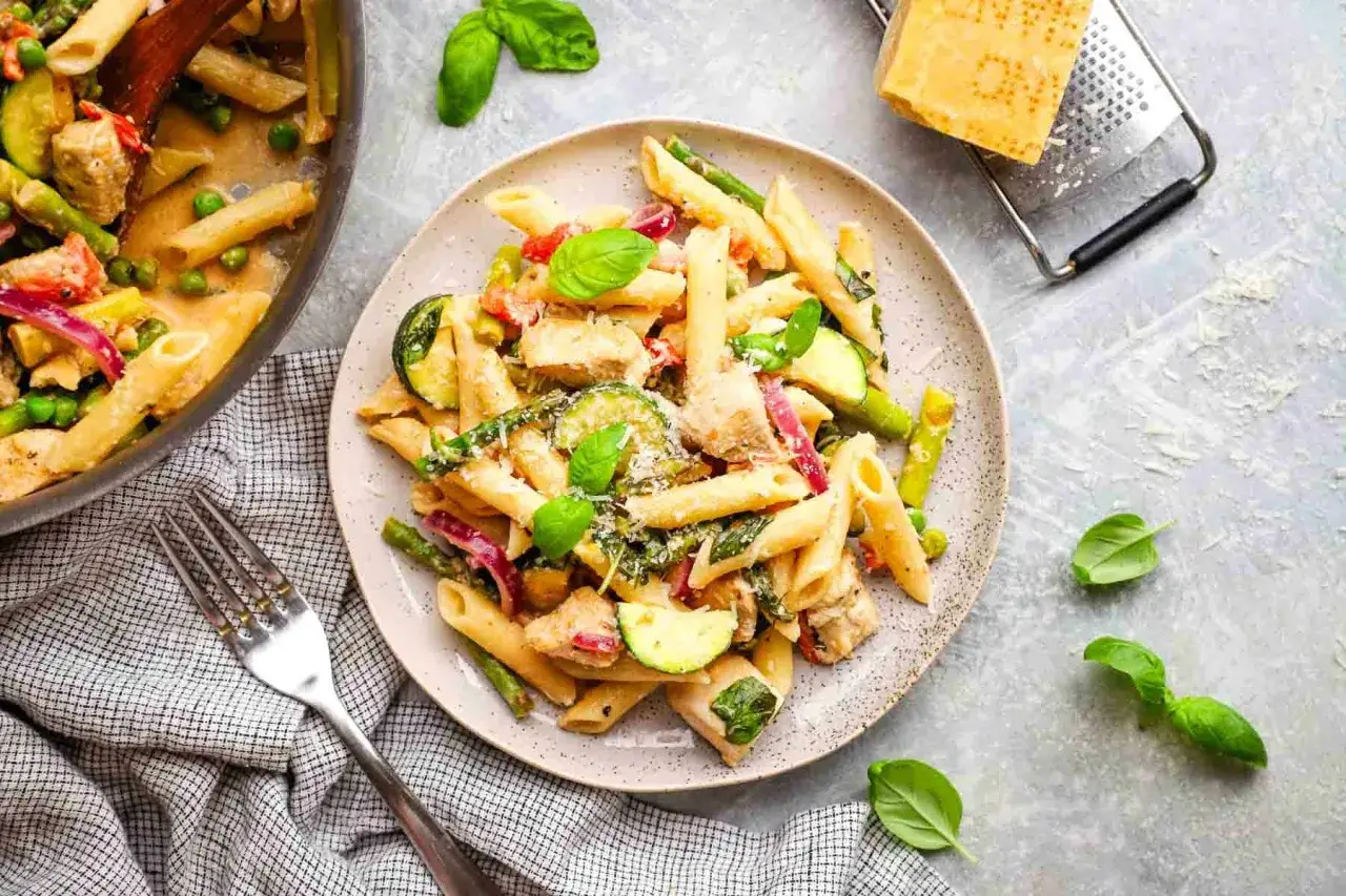 Penne con pollo, zucchine, asparagi e piselli, un gustoso condimento pasta per dieta, guarnito con basilico fresco e parmigiano.