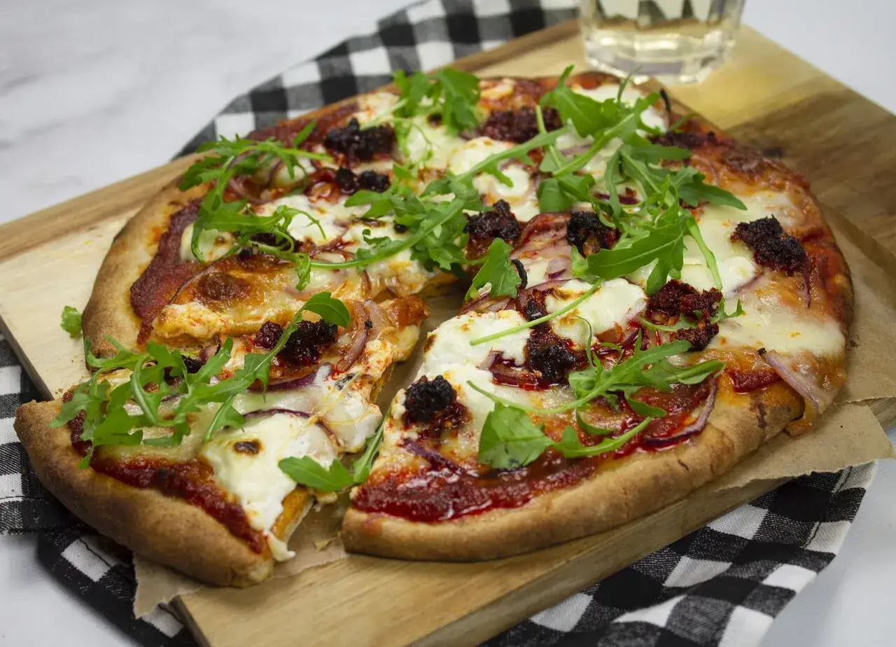 Pikantna pizza nduja z mozzarellą, rukolą i czerwoną cebulą, podana na desce.