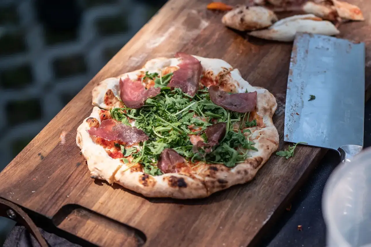 Pyszna pizza na kamieniu z rukolą i szynką, gotowa do pokrojenia.