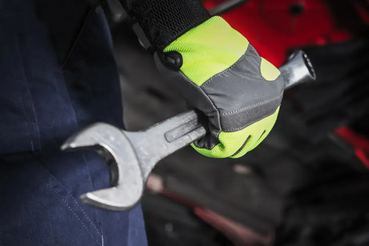 Mano enguantada con equipo de protección individual, sujetando una llave inglesa para reparar un motor.