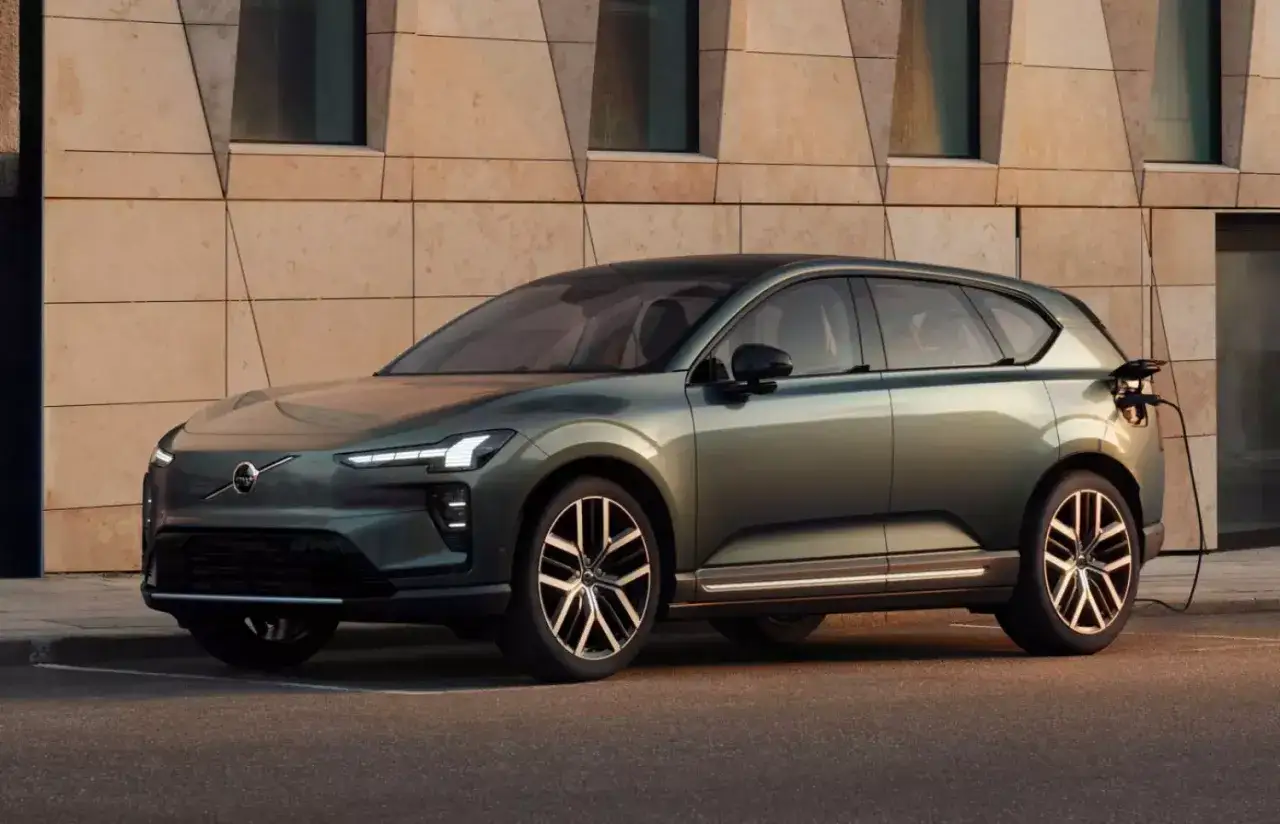 Nowoczesny, zielony Volvo EX60 ładuje się przy nowoczesnym budynku.