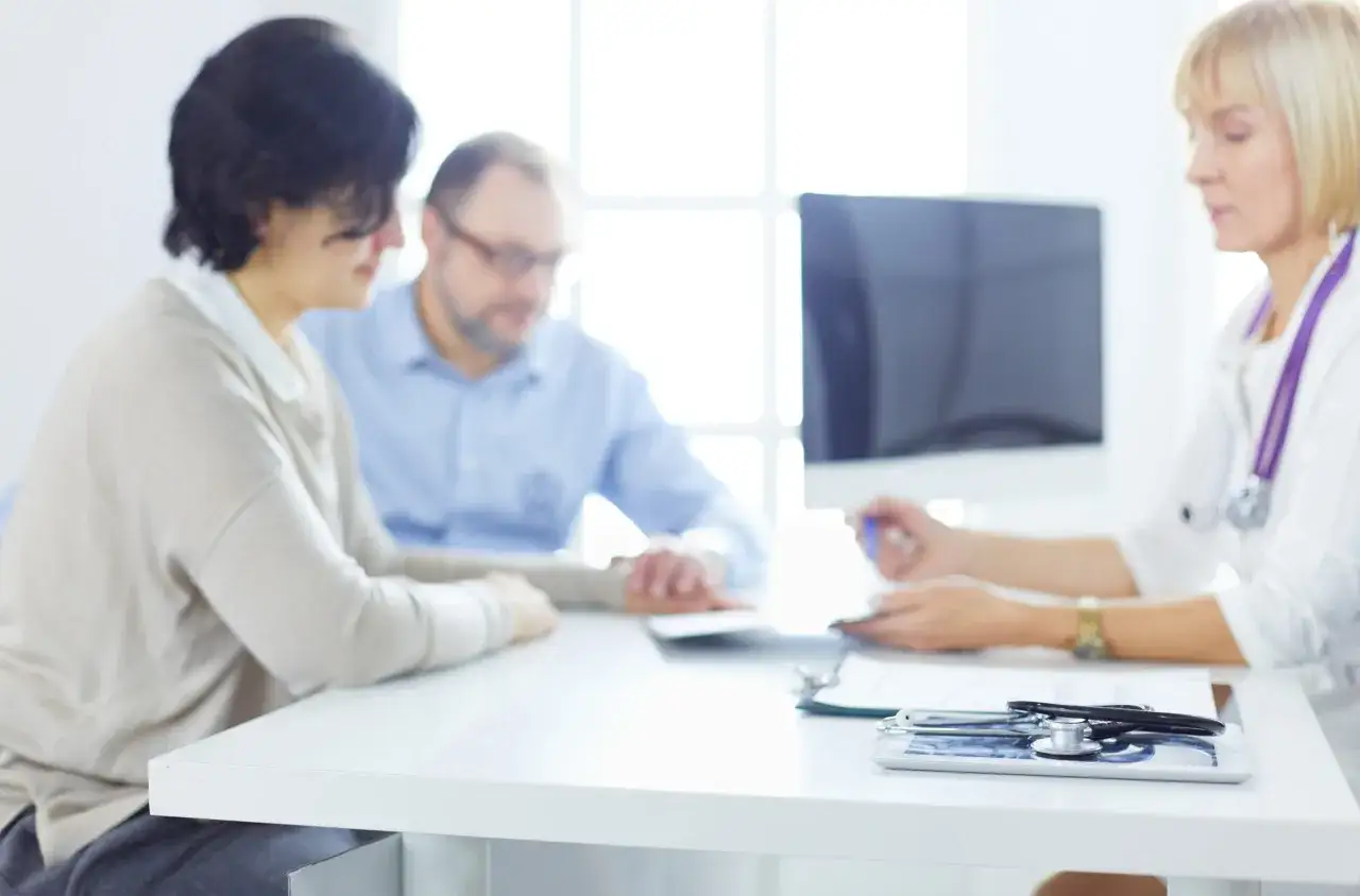 Medico e pazienti discutono, evidenziando una comunicazione medico paziente efficace. Sul tavolo, uno stetoscopio e una cartella clinica.