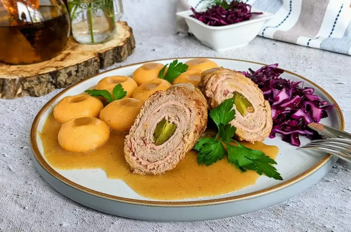 Pyszna rolada wołowa z ogórkiem kiszonym, podana z kluskami śląskimi i czerwoną kapustą.