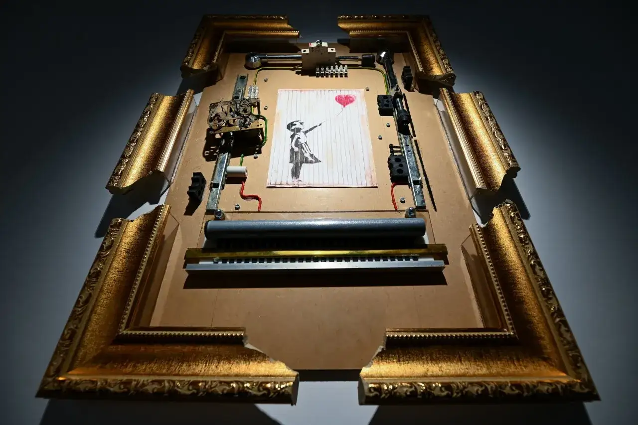 Słynne dzieło Banksy'ego, dziewczynka z balonikiem, w złotej, pękniętej ramie z ukrytym mechanizmem.