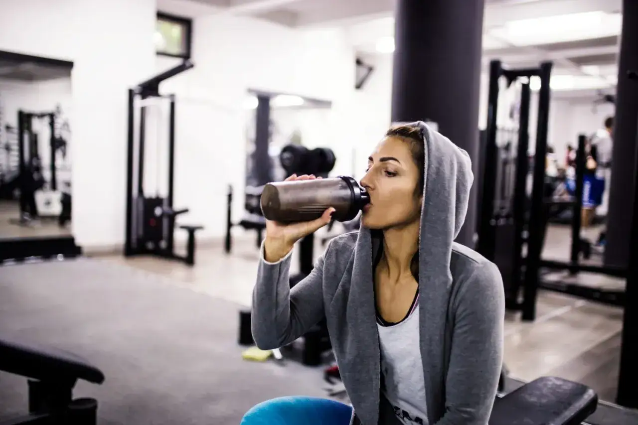 Frau trinkt nach dem Training einen Proteinshake im Fitnessstudio.