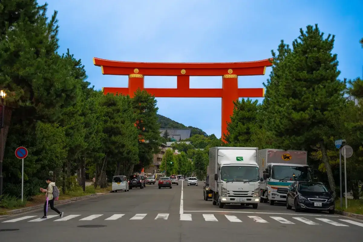 Droga pod wielką, czerwoną bramą torii, otoczona drzewami. Ciekawe ciekawostki o Japonii czekają za tym symbolicznym przejściem.
