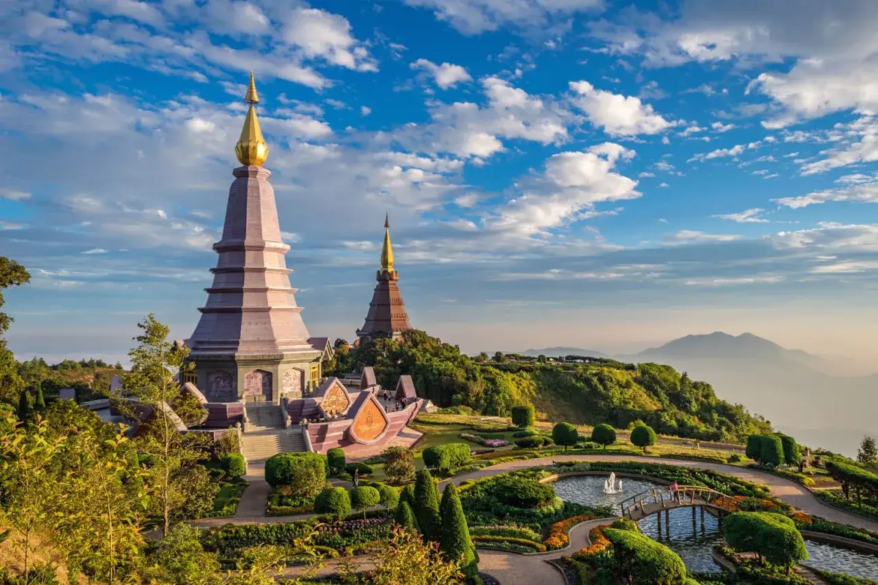 Zwei goldene Pagoden thronen auf einem gr&uuml;nen H&uuml;gel, umgeben von einem bl&uuml;henden Garten mit Teich und Br&uuml;cke. Ein Traumziel f&uuml;r 4 Wochen Thailand.