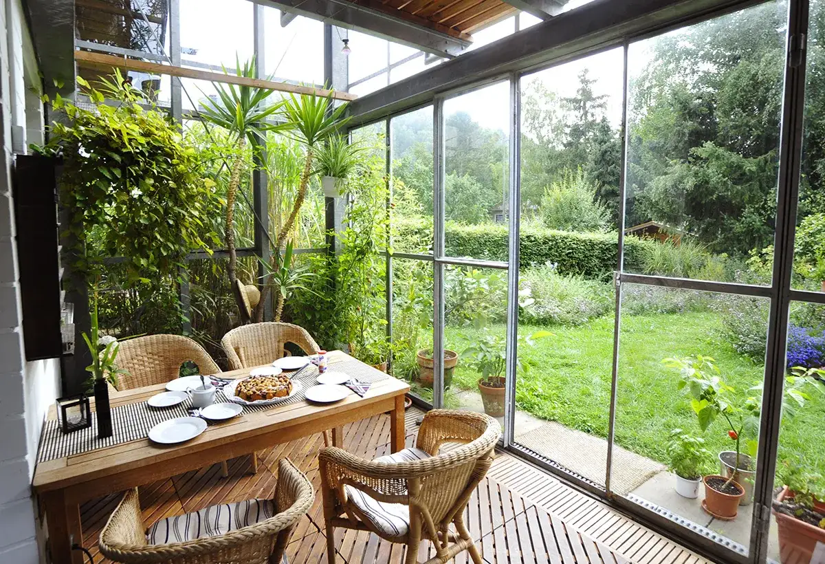 Une table en bois et des chaises en rotin dans une v&eacute;randa lumineuse, offrant une belle id&eacute;e am&eacute;nagement petite v&eacute;randa avec vue sur un jardin verdoyant.