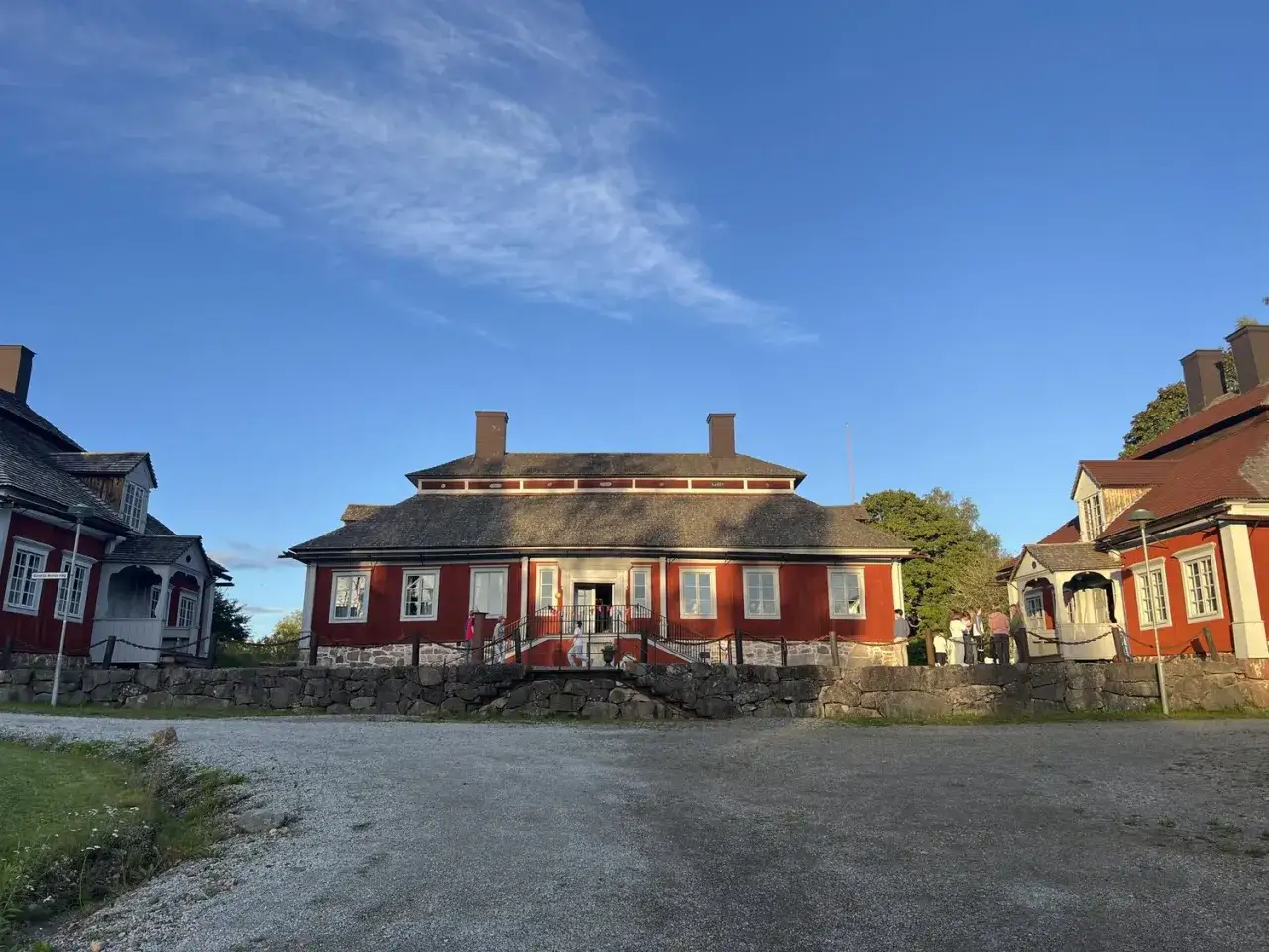 Malingsbo herrg&aring;rd i solnedg&aring;ngen. R&ouml;da byggnader med vita knutar och gr&aring; tak. En steng&auml;rdesg&aring;rd avgr&auml;nsar g&aring;rdsplanen.