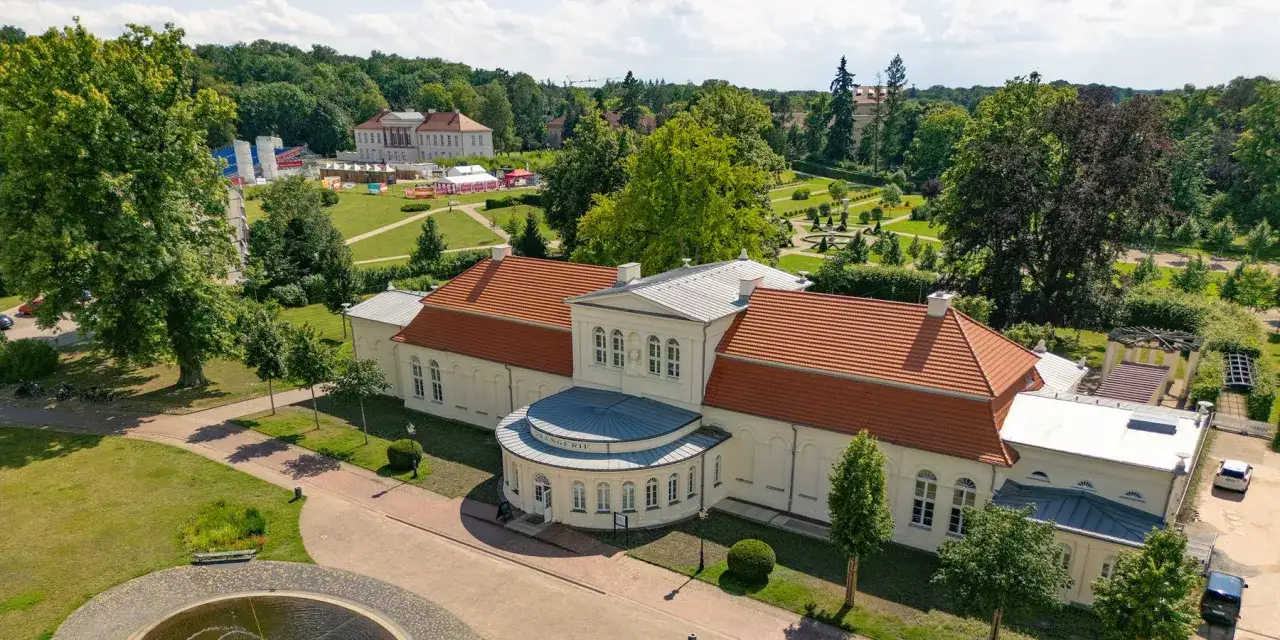 Die Orangerie Ludwigslust, ein prächtiges Gebäude mit roten Ziegeldächern, umgeben von einem weitläufigen Park mit Bäumen und gepflegten Gärten.