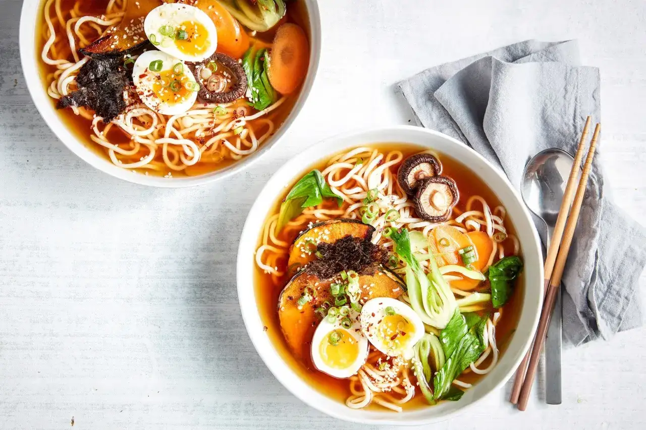 Zwei Schalen dampfender vegetarischer Ramen mit Nudeln, Ei, Pilzen, K&uuml;rbis und Gem&uuml;se.