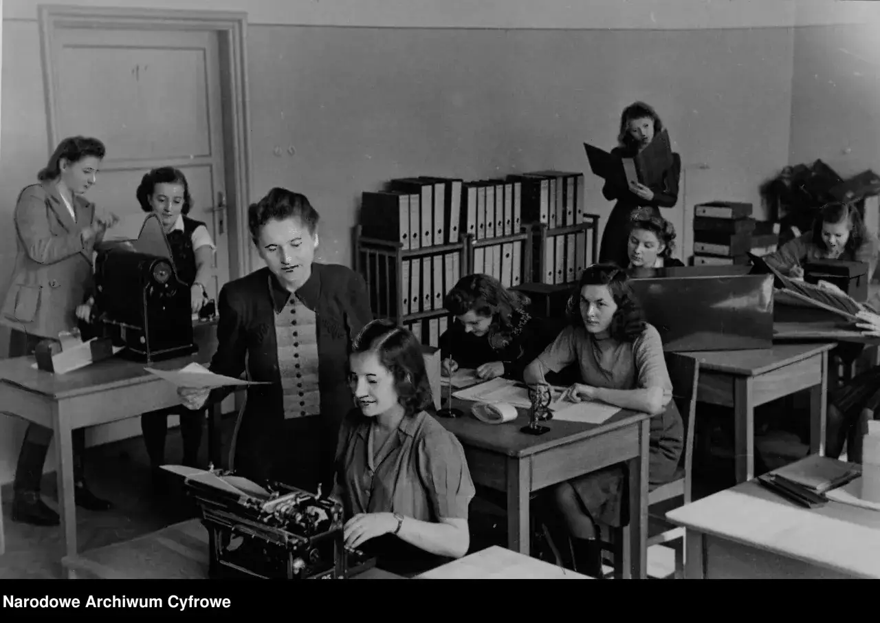 Kobiety pracujące w biurze, jedna przy maszynie do pisania, inne nad dokumentami. To właśnie tajne komplety, czyli tajne nauczanie, które odbywało się w ukryciu.
