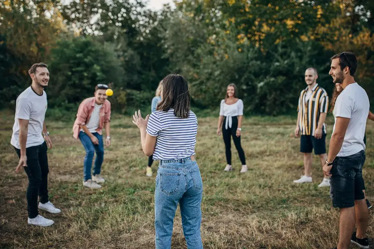 Un grupo de adolescentes se divierte al aire libre, lanzando una pelota amarilla. Son juegos para adolescentes llenos de risas y buen ambiente.