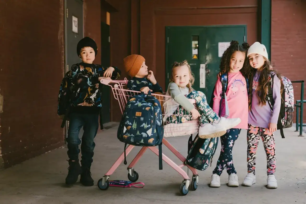 Cinq enfants, prêts pour la photo de classe, portent des tenues colorées et des sacs à dos amusants.