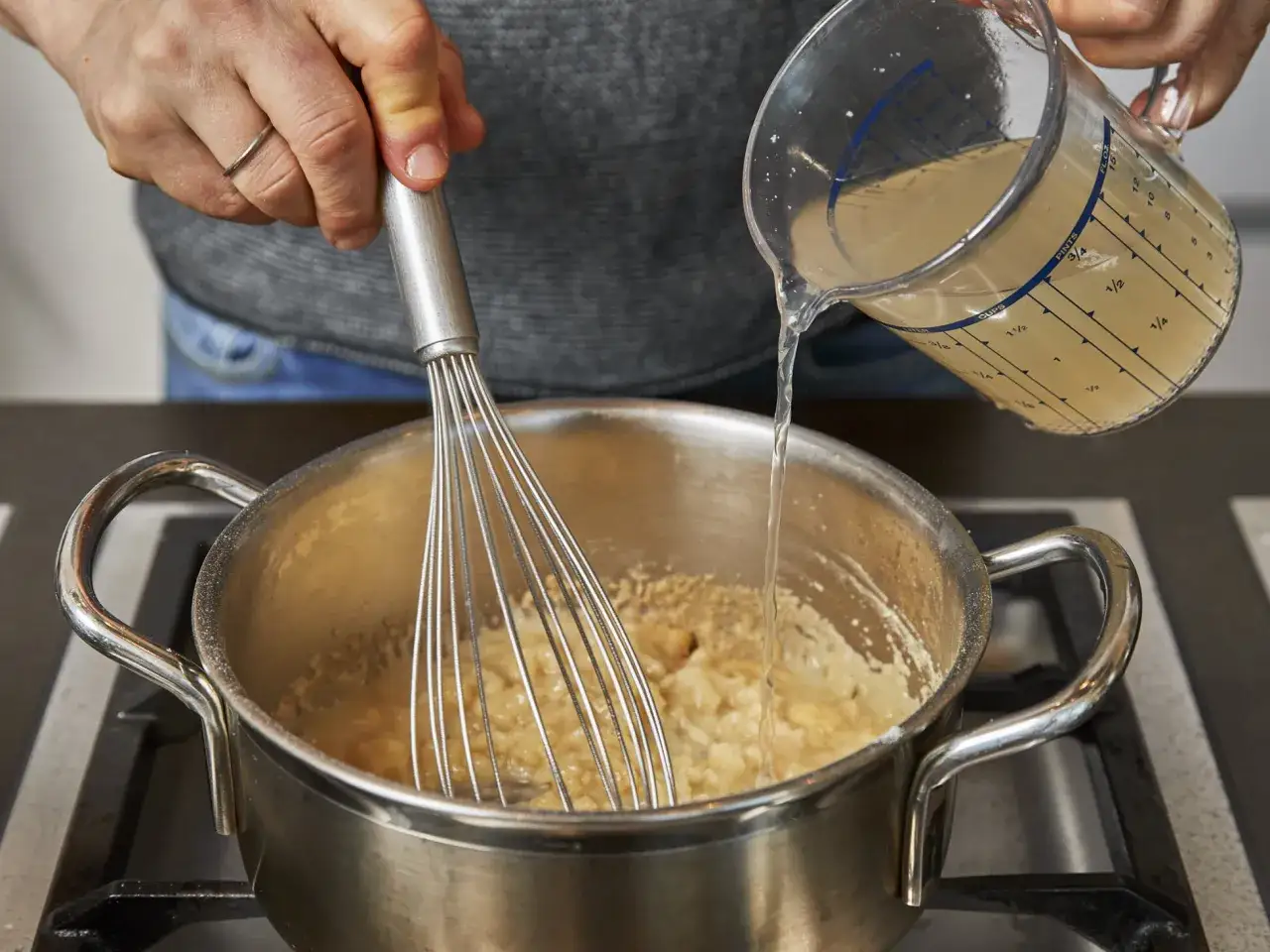 Flüssigkeit wird in eine Pfanne gegossen, während mit einem Schneebesen gerührt wird, um eine Mehlschwitze zu machen.
