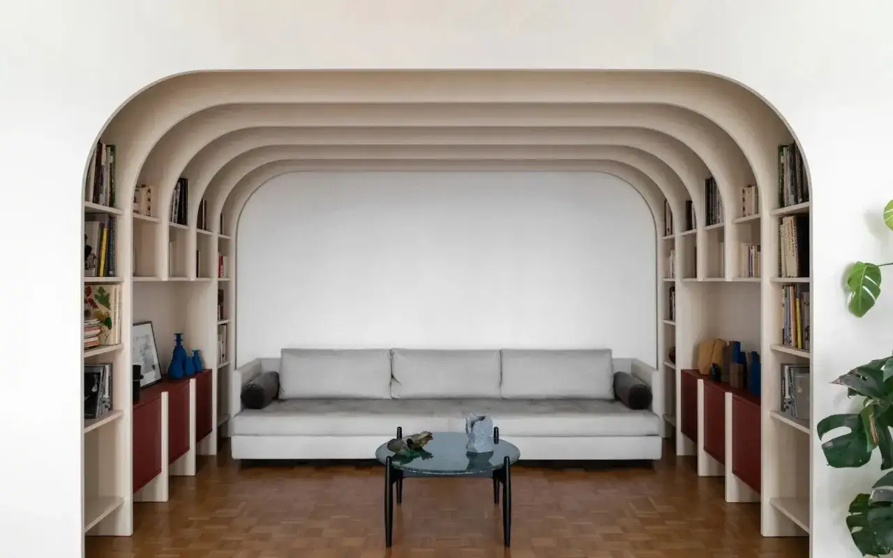 Un salon moderne avec un canapé gris, une table basse ronde et des étagères intégrées dans une arche de maison.