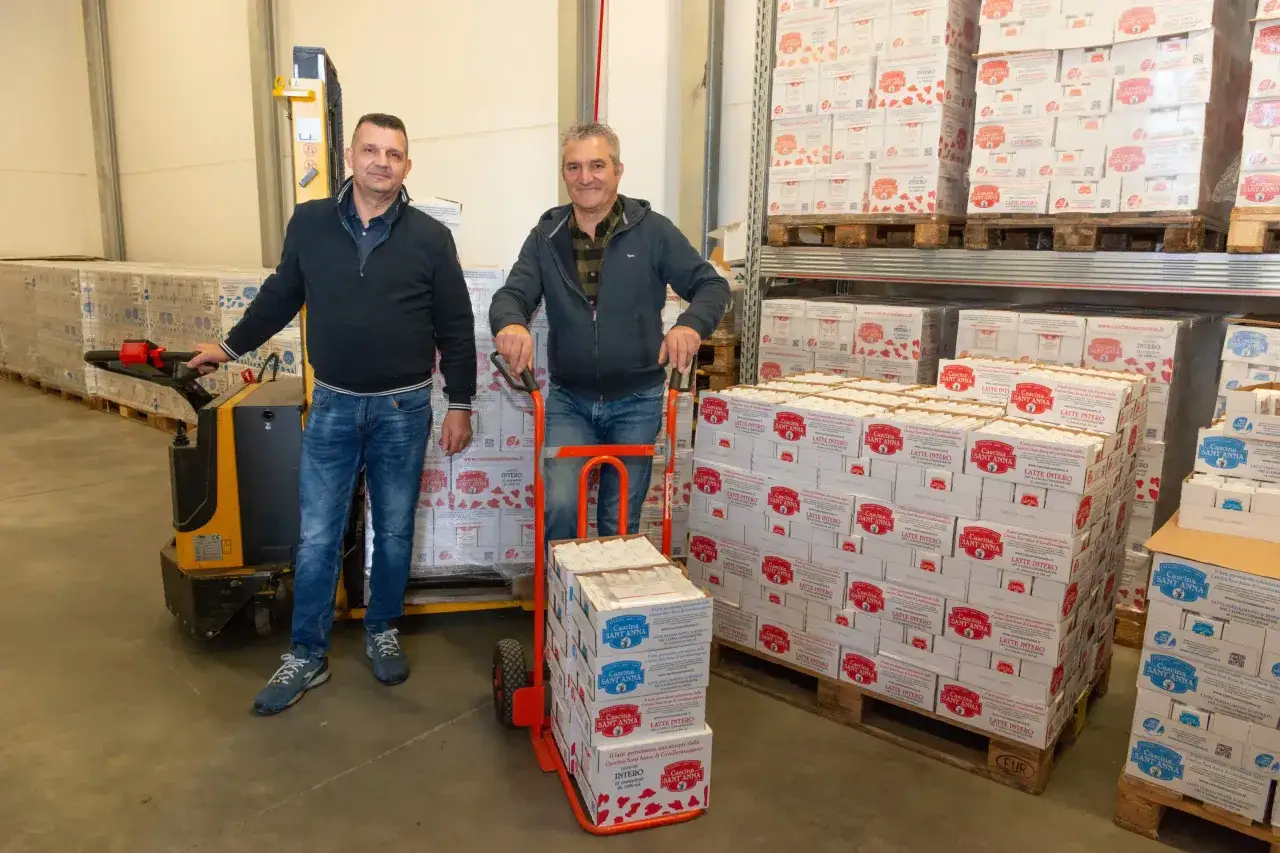 Due uomini in un magazzino con scatoloni di latte a lunga conservazione aperto fuori dal frigo.