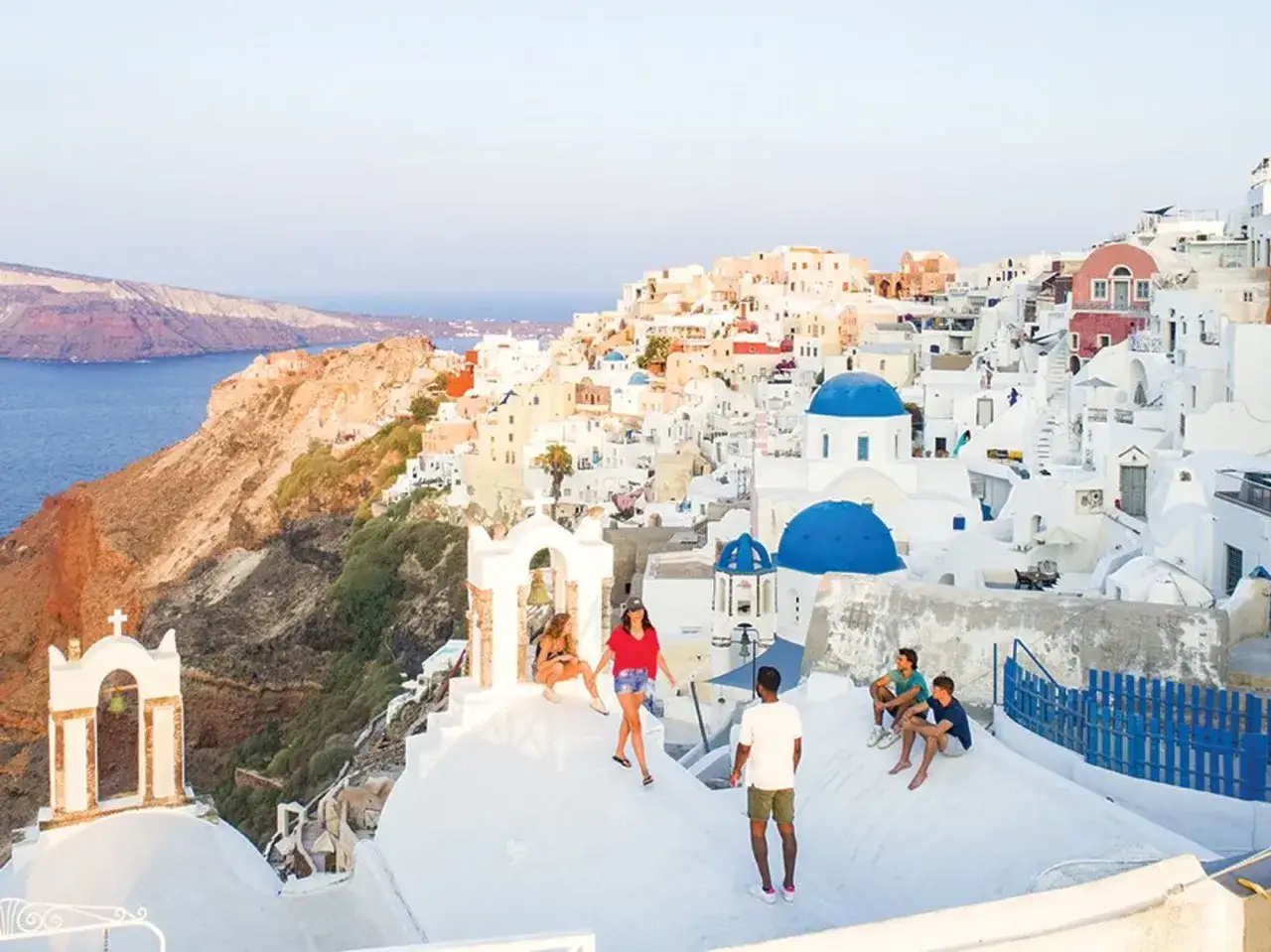 Friends enjoy a sunny day on a gay Greek island, with iconic white buildings and blue domes overlooking the sea.