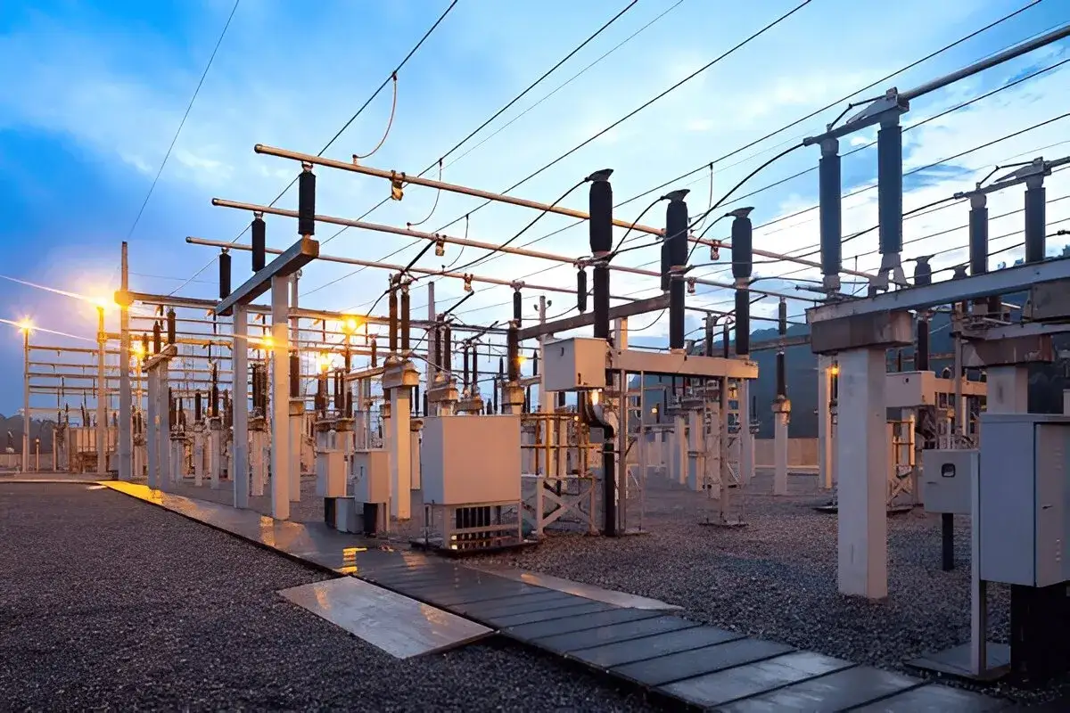 Rozległa sieć energetyczna z licznymi izolatorami i przewodami, oświetlona ciepłym światłem lamp.