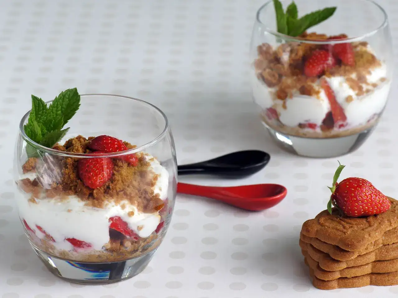Délicieux dessert fraise mascarpone en verrine, garni de crumble et d'une feuille de menthe. Une fraise trône sur une pile de biscuits.