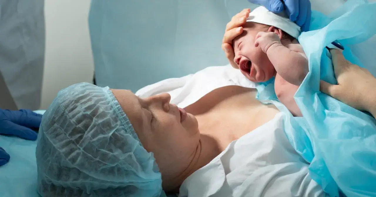 Nowy człowiek na świecie! Mama patrzy na swoje dziecko tuż po porodzie. To początek pięknego połogu.