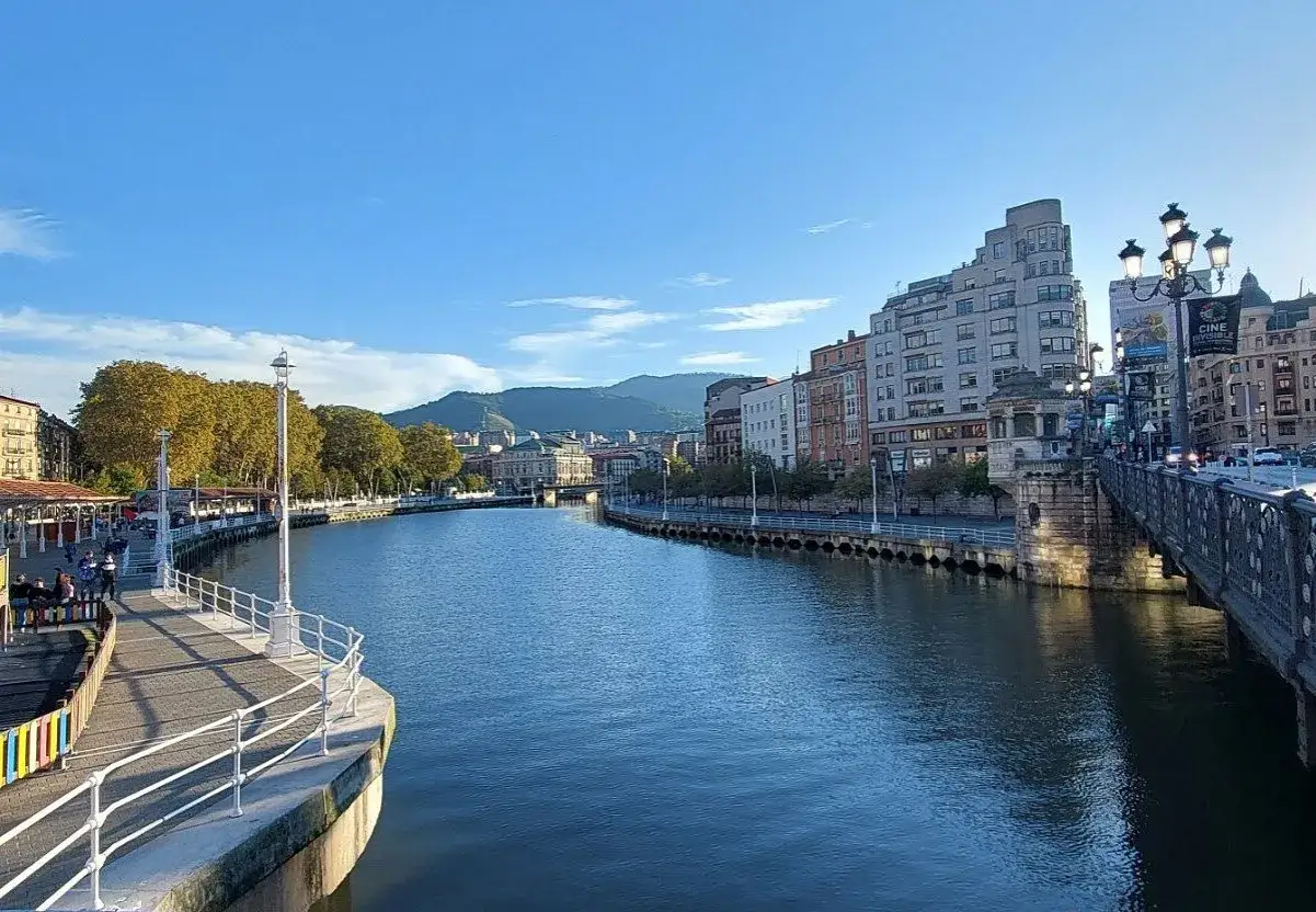 Der Bilbao Fluss flie&szlig;t ruhig durch die Stadt, ges&auml;umt von historischen Geb&auml;uden und gr&uuml;nen B&auml;umen.