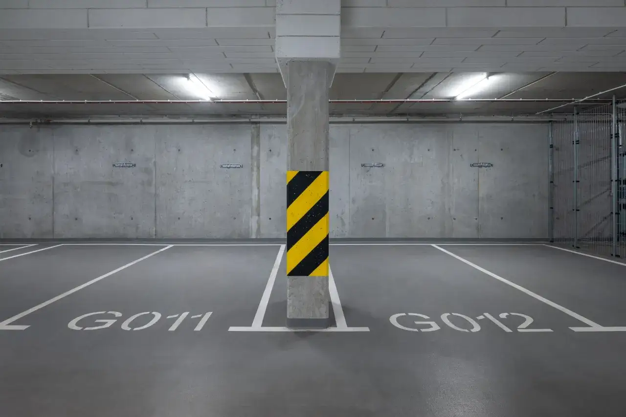 Puste miejsce parkingowe G011 i G012 w garażu podziemnym. Betonowe ściany i sufit, oświetlenie jarzeniowe.
