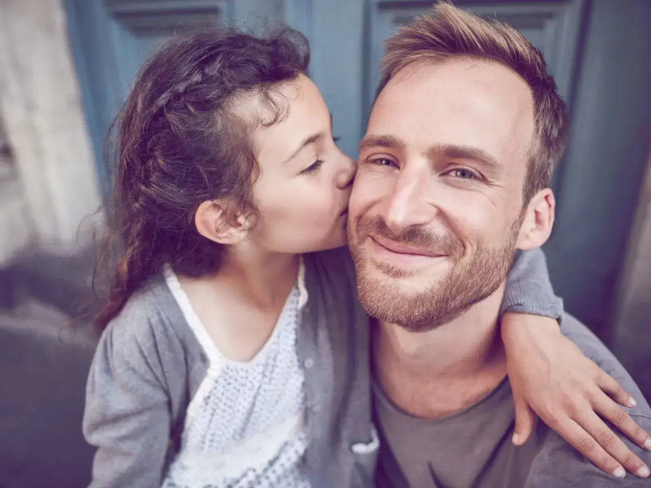 Ein kleines M&auml;dchen k&uuml;sst ihren Vater auf die Wange. Diese liebevolle vater-tochter beziehung beeinflusst die Partnerschaft positiv.
