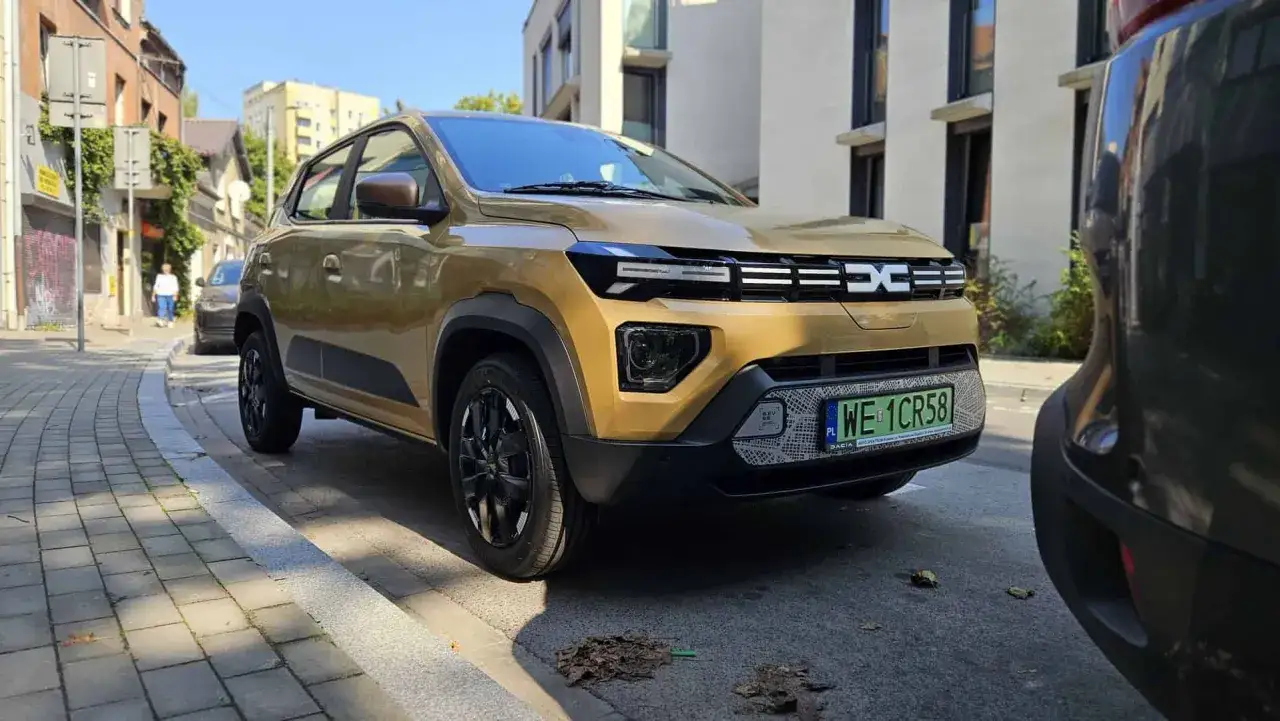 Złota, nowa Dacia Spring stoi na ulicy, gotowa na miejskie wyzwania.