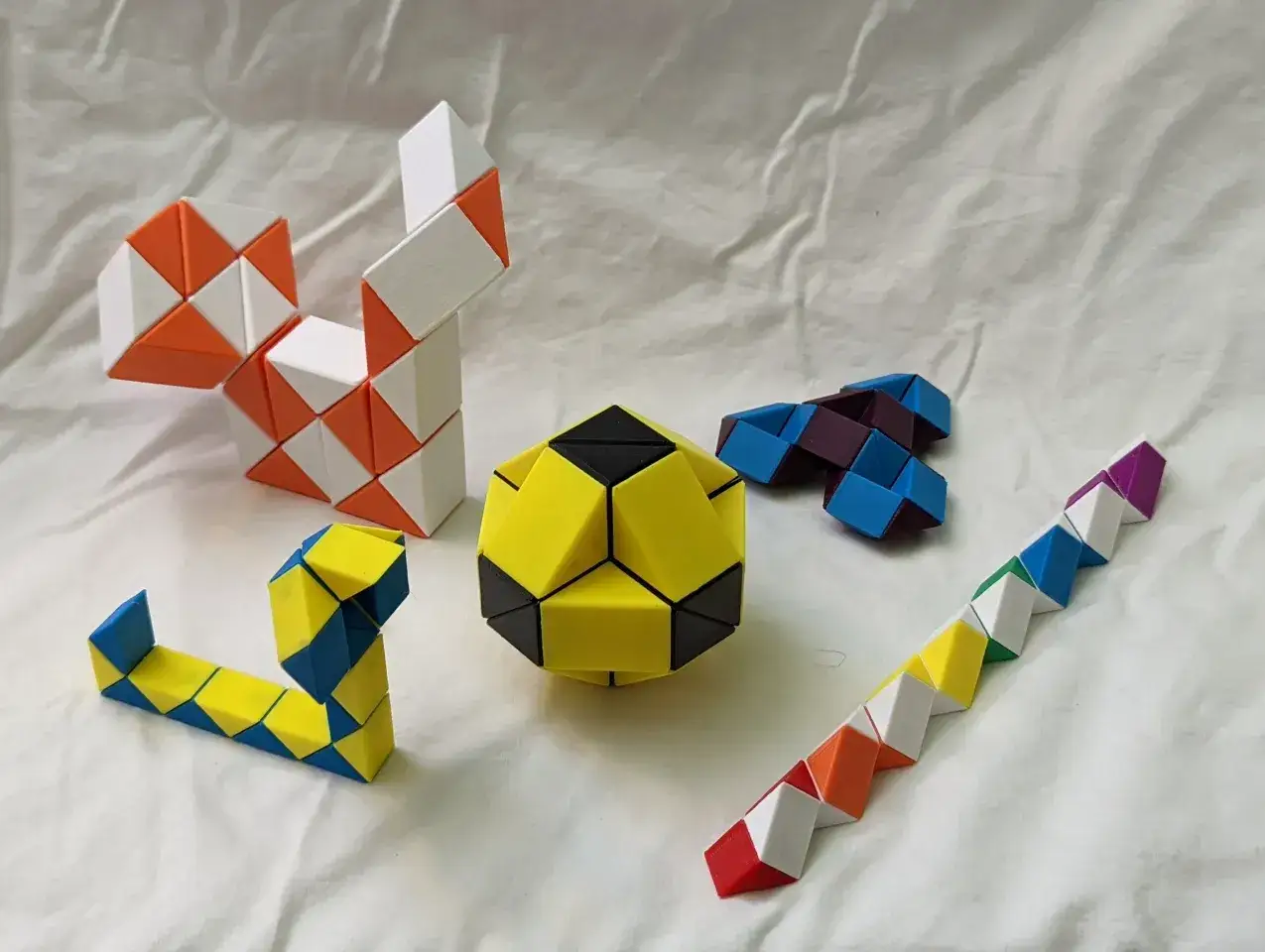Flera färgglada rubiks ormar och en bollformad pusselbit ligger utspridda på en vit bakgrund.