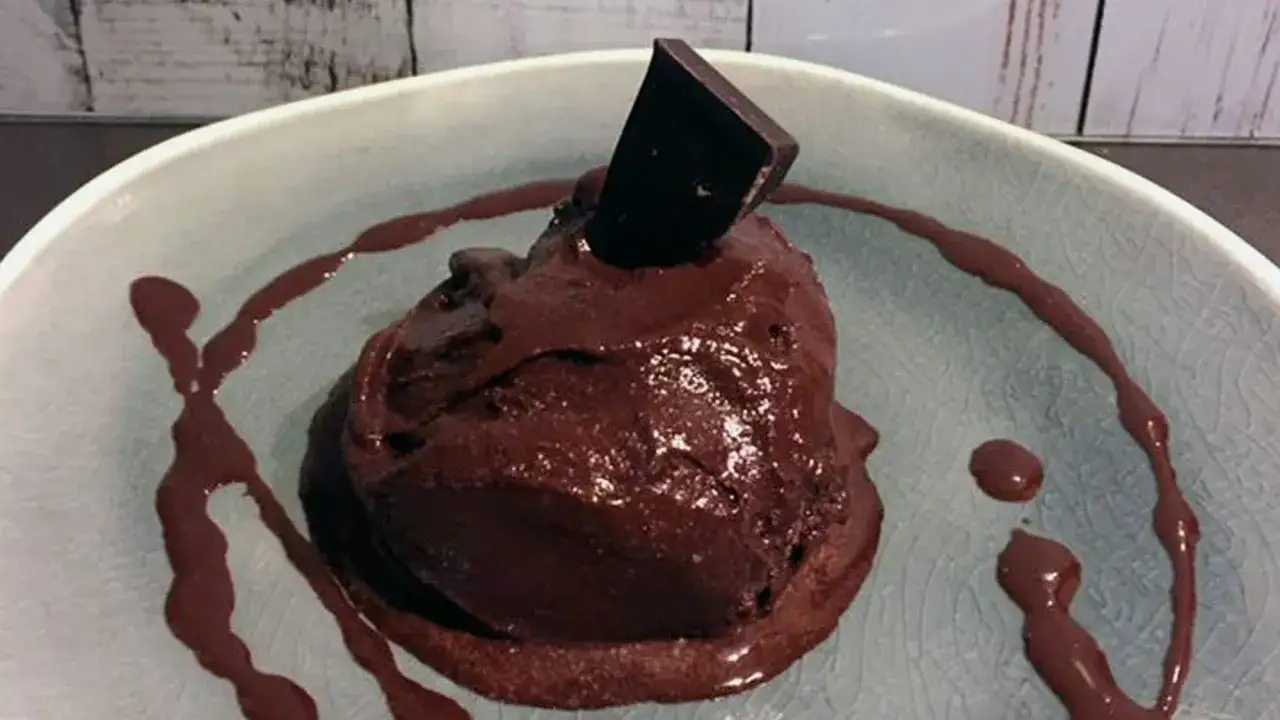 Schokoladen-Bier-Eis mit einem Stück dunkler Schokolade obendrauf, serviert in einer Schale mit Schokoladensauce.
