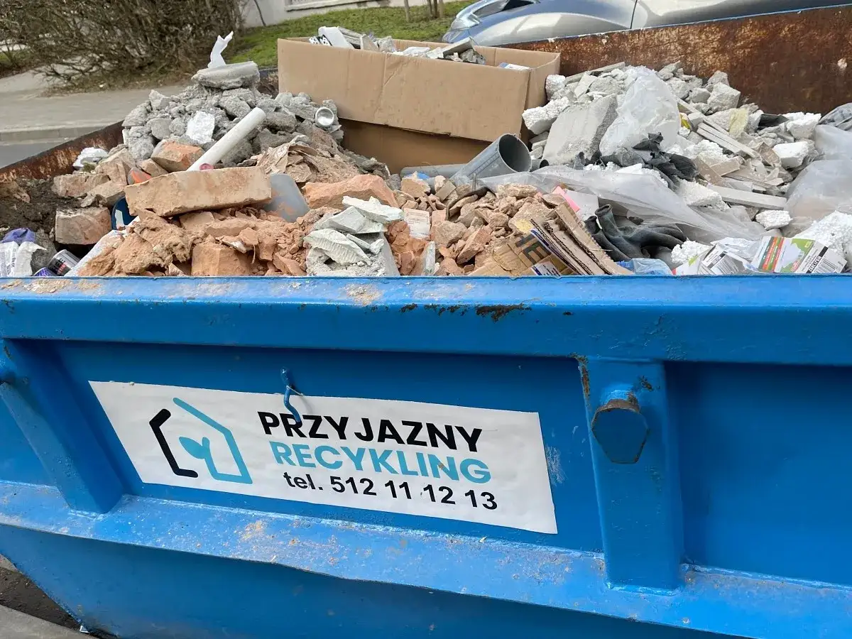 Kontener z gruzem budowlanym, cegłami i betonem. Na niebieskim kontenerze widnieje napis