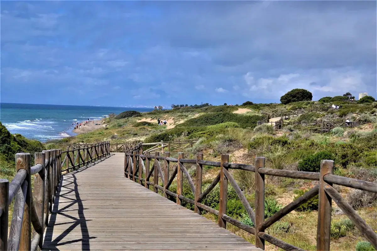 Holzsteg f&uuml;hrt zum Strand an der Costa del Sol. D&uuml;nen und Vegetation s&auml;umen den Weg.