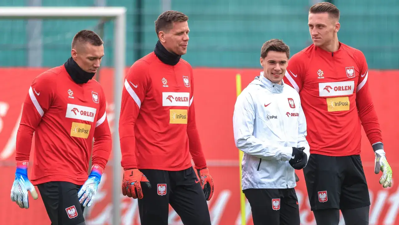 Bramkarze reprezentacji Polski w czerwonych strojach i jeden w białej kurtce, gotowi do treningu.