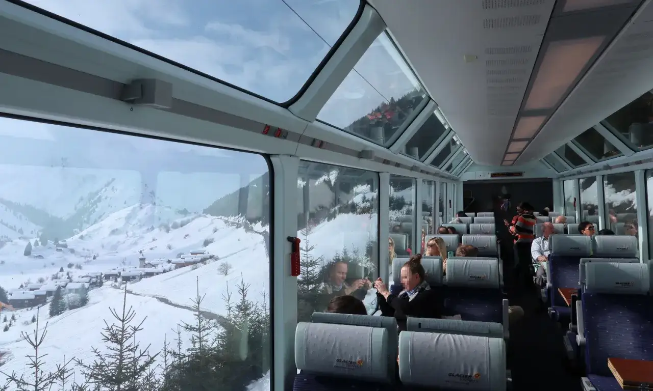 Blick aus dem Panoramawagen eines Glacier Express. Eine Schweiz Rundreise Zug durch verschneite Alpenlandschaft mit kleinen D&ouml;rfern.